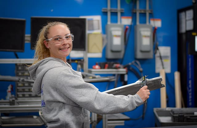 Mallory measures a part at her company during her apprenticeship.
