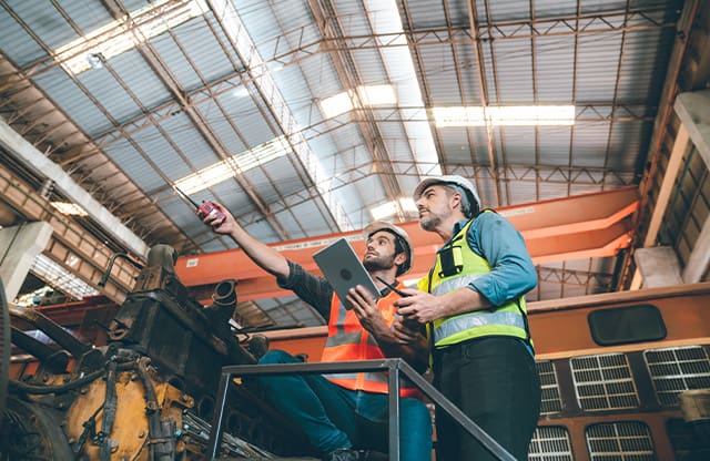 Two men review work progress in a manufacturing company using a tablet.