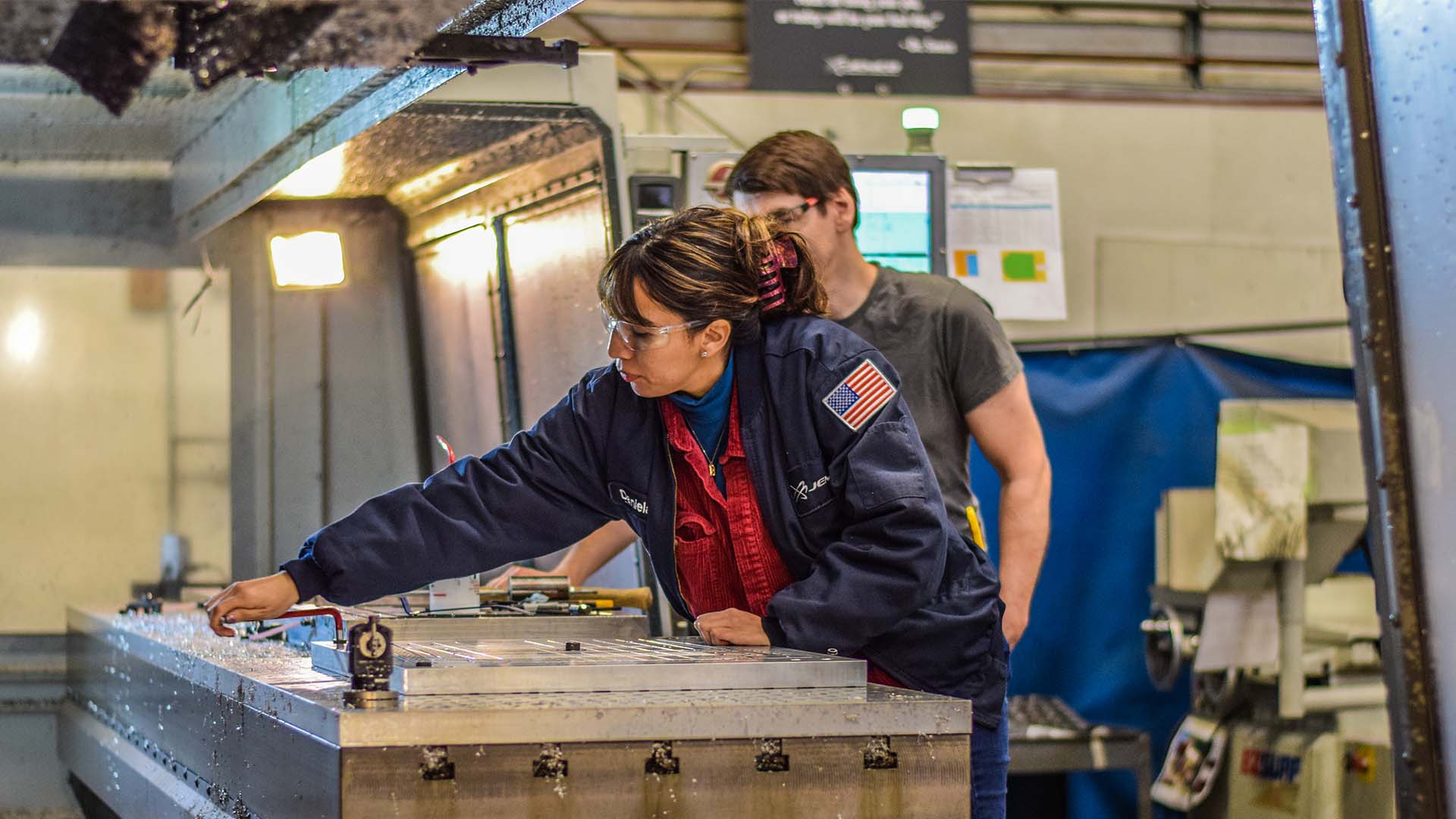 An apprentice learn from her mentor on the shop floor at a machine shop.