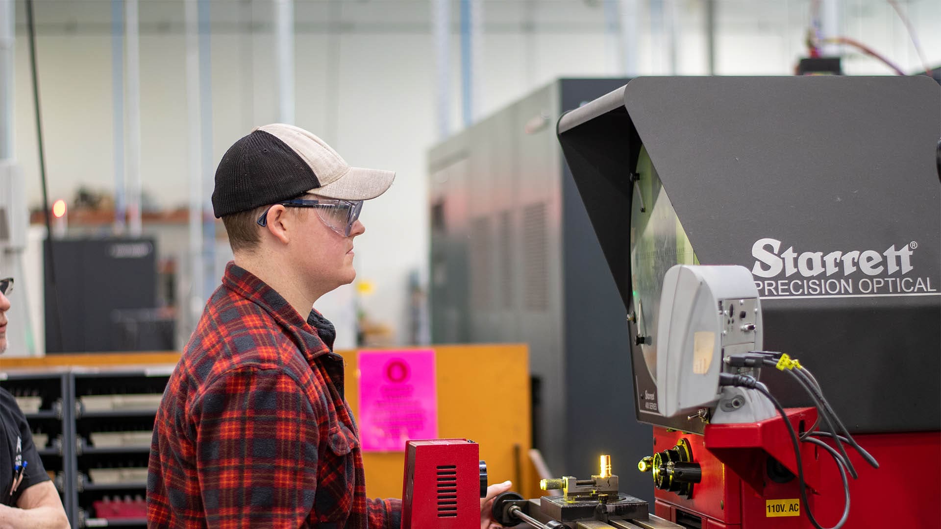 WorkEx intern uses equipment to test a machined part while his supervisor looks on.