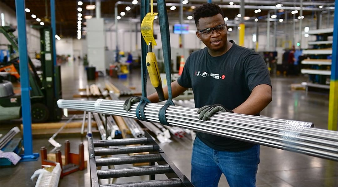 Luke Bizimungu moves a piece of stock material to be cut on a bandsaw at Automatic Products