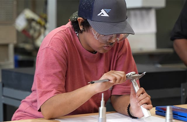 A Manufacturing Academy student uses a caliper during class.