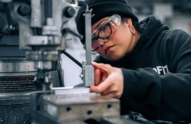 A student in the Manufacturing Academy learns how to measure a part on a manual milling machine.