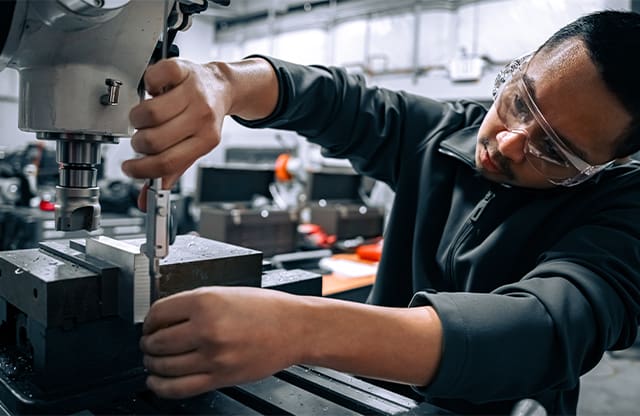A Manufacturing Academy student measures a part on a manual milling machine.
